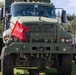 A front-facing view of a military olive-drab Mack truck displayed at what appears to be an outdoor public event or show. The vehicle bears U.S. Army markings and a red flag with '500' attached to the front. Spectators and other vehicles are visible in the background.
