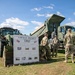 A group of U.S. Army soldiers in OCP camouflage uniforms are gathered around military engineering equipment at an outdoor display. A whiteboard sign identifies the display as related to 'Airfield Pegnitz EDQZ,' built by the U.S. Army in 1974, associated with the 130th Engineer Brigade and 535th Engineer Company. The scene appears to be a static equipment demonstration or open house event on a grassy field.