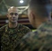 A U.S. Marine officer with the name tape 'MARTINEZ' and gold oak leaf cluster insignia (indicating the rank of Major) is engaged in conversation with other Marines in what appears to be an indoor military facility or gymnasium. He is wearing the standard Marine Corps MARPAT woodland camouflage uniform. The image captures an informal briefing or discussion among military personnel.