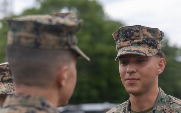 Two U.S. Marines in MARPAT (Marine Pattern) digital camouflage uniforms are engaged in a face-to-face conversation. The Marine facing the camera has a name tape reading 'TABORDA' and a 'U.S. MARINES' branch tape visible on his uniform. The setting appears to be an outdoor military area with tents and vehicles in the background.