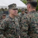 A group of U.S. Marines in MARPAT woodland digital camouflage uniforms are gathered outdoors near a white tent structure. The central figure, identified by a name tape reading 'WATSON,' appears to be a senior officer with two stars visible on the collar, indicating the rank of Major General. He is engaged in a face-to-face conversation with another Marine whose back is to the camera.