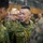 The image shows a group of military personnel in what appears to be an indoor briefing or meeting environment. The central figure is wearing Japanese Ground Self-Defense Force (JGSDF) camouflage uniform with a name tape reading 'ARAI' and rank insignia visible. Personnel from what appears to be both JGSDF and U.S. Marine Corps are present, suggesting a joint military exercise or coordination event.