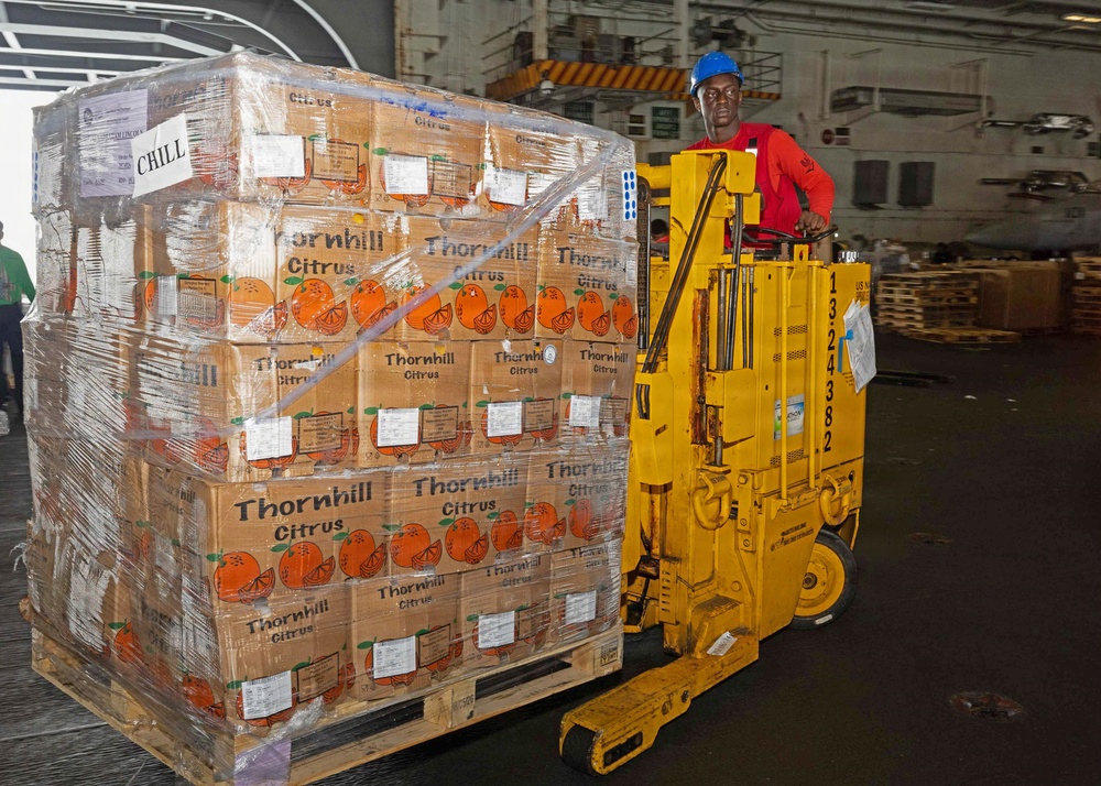 A worker wearing a blue hard hat and red shirt operates a yellow electric pallet jack/forklift inside what appears to be a large warehouse or ship cargo hold. The pallet being transported is stacked with multiple layers of cardboard boxes branded 'Thornhill Citrus,' wrapped in clear plastic stretch film. A 'CHILL' label is visible on the pallet, indicating the cargo requires refrigeration.