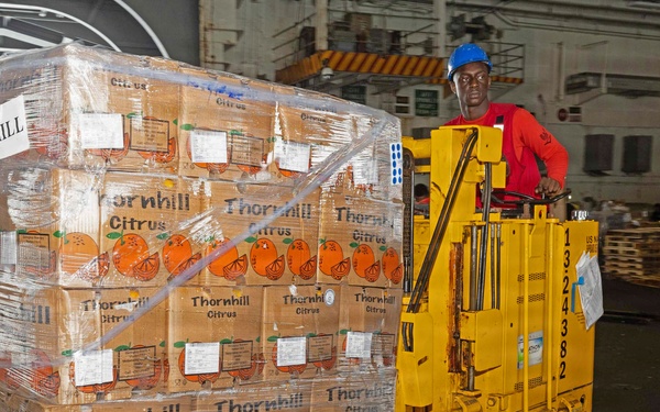 A worker wearing a blue hard hat and red shirt operates a yellow electric pallet jack/forklift inside what appears to be a large warehouse or ship cargo hold. The pallet being transported is stacked with multiple layers of cardboard boxes branded 'Thornhill Citrus,' wrapped in clear plastic stretch film. A 'CHILL' label is visible on the pallet, indicating the cargo requires refrigeration.