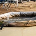 The image shows a military-style collapsible fabric water storage tank or blivet being filled with water via a pipe or hose. Water is actively flowing into the circular, canvas-walled portable reservoir, which is secured with rope or cord ties. The setting appears to be a field operations or training environment with sandy/dirt terrain and equipment visible in the background.