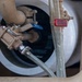 The image shows a close-up of a plumbing assembly, likely associated with a water heater or pressure regulation system. Multiple valves, fittings, and flexible hoses are visible, including a bronze/brass pressure reducing valve and a blue-handled ball valve. The setup appears to be a residential or light commercial water supply connection point.