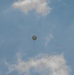 A single white/light-colored spherical balloon is visible ascending through a partly cloudy blue sky. A small payload or instrument package appears to be suspended beneath the balloon via a thin line or cord. The image appears to depict a weather or radiosonde balloon used for atmospheric data collection.