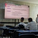 A military training or educational session is taking place in a classroom setting, with a U.S. Army soldier in camouflage uniform presenting a 'Terminal Learning Objective' slide about civil engagements. The audience consists of several military personnel in white naval/dress uniforms, and a senior officer in white uniform stands to the right near a banner. The presentation includes flags of Tunisia and the United States, suggesting a multinational military cooperation exercise.