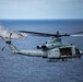 A U.S. Marines helicopter, identified as a UH-1Y Venom (serial number 168508), is flying over open ocean with its side door open and crew visible inside. In the background, a vessel appears to be on fire or producing significant smoke, suggesting a maritime exercise or incident response scenario. The image is sharp and well-composed, captured from another airborne platform.