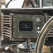 A ruggedized military-grade electronic display unit mounted on what appears to be a vehicle or equipment platform. The small OLED or LCD screen displays the text 'END OF MISSION' in white characters on a black background. The unit features vibration-isolation wire rope mounts on both sides and navigation buttons, consistent with field-use military hardware.