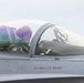 A military pilot is seated in the cockpit of a fighter jet, wearing a flight helmet and olive green flight suit. The aircraft fuselage displays the text 'SGTMAJ J.A. MABE' in red lettering, indicating the crew chief or dedicated crew member's name. The canopy is closed and the pilot appears to be preparing for or returning from a flight.