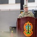 A U.S. Army soldier identified by name tape as 'ZIMMER' stands at a wooden podium bearing a military unit insignia with the motto 'Safe, Secure, Reliable.' The soldier appears to be delivering a speech or remarks at an official military ceremony or event. A second soldier stands in the background to the right.