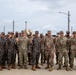A group of approximately 20-25 military personnel from two distinct forces are posing together for a group photo outdoors. The soldiers are wearing two different camouflage uniform patterns, consistent with U.S. Army MultiCam/OCP and Republic of Korea (ROK) Army digital camouflage uniforms. Many individuals are raising their fists in a unified gesture, suggesting a joint military exercise or cooperative event.