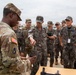 A U.S. Army soldier is conducting a demonstration or briefing for a group of Republic of Korea (ROK) Army personnel at what appears to be a joint military exercise or equipment showcase. The U.S. soldier, wearing OCP (Operational Camouflage Pattern) uniform with an American flag patch, is presenting a piece of equipment to attentive ROK military officers and soldiers. This appears to be a bilateral military cooperation event between U.S. and South Korean forces.