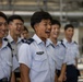 A group of young personnel in light blue military or aviation uniforms are standing in a row, laughing and smiling. The individuals wear wing-shaped badges on their chest pockets and rank insignia on their shoulders, suggesting an aviation or air force context. The mood is visibly joyful and relaxed.