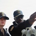 Three U.S. Navy personnel are photographed on the deck of USS John Finn (DDG-113), a guided-missile destroyer. A senior sailor appears to be pointing and giving instruction or direction to a junior sailor, while a third crew member holds a radio or communication device in the background. All three are wearing USS John Finn ship's company ball caps.