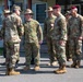 A group of multinational military personnel are gathered outdoors in front of a building, appearing to be engaged in informal conversation. The group includes soldiers wearing different uniform styles and headgear, suggesting a joint or combined military exercise or meeting. Japanese Ground Self-Defense Force personnel are visible alongside what appear to be U.S. Army and Australian Defence Force soldiers.