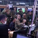 A joint military operations center showing personnel from what appears to be the U.S. Army and Japan Ground Self-Defense Force (JGSDF) gathered around workstations during what appears to be a combined exercise or briefing. A U.S. Army officer in MultiCam uniform is seated at a desk marked 'Fires Director COL WHEATLEY' while surrounded by numerous JGSDF personnel in Japanese camouflage uniforms. The setting is a command and control facility with multiple computer monitors, cables, and communications equipment.