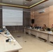 A multinational military briefing or planning meeting is taking place in a conference room, with personnel from what appears to be Indonesian military (TNI AU) and U.S. military (PACAF) seated at arranged tables. A presentation titled 'Air Medical Evacuation Plan' is displayed on a projection screen at the front of the room. The setting suggests a bilateral or multilateral military cooperation exercise or planning session.