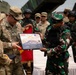A military ceremony showing U.S. Army personnel presenting a commemorative plaque to an Indonesian military officer. The plaque features both the Indonesian and American flags, suggesting a joint military exercise or partnership event. Multiple soldiers from both nations are visible in the background.