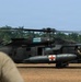 A military medical evacuation (MEDEVAC) UH-60 Black Hawk helicopter marked 'Arctic Dustoff' is on the ground at what appears to be a tropical location. A soldier wearing a red cross-marked shirt and helmet is observing the helicopter from the foreground. The aircraft bears red cross markings indicating its medical/MEDEVAC role.