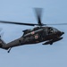 A United States Army UH-60 Black Hawk helicopter configured as a medevac (medical evacuation) aircraft is captured in flight against an overcast blue-gray sky. The helicopter displays prominent red cross markings on its fuselage, identifying it as a medical transport. The rotor blades show motion blur, indicating active flight.