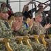 A group of military officers from at least two different nations are seated in ornate gold chairs at what appears to be an official military ceremony or demonstration. Three senior officers in the foreground are applauding, with two wearing camouflage uniforms bearing star insignia and one wearing a US Army uniform with a 101st Airborne Division patch. Civilians and additional military personnel in the background are photographing the event with cameras and smartphones.