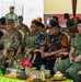 A multinational military gathering showing officers and officials from multiple nations seated in ornate golden chairs under a tent canopy. Visible name tags and uniform patches identify representatives from the U.S. Army, TNI AD (Indonesian Army), and Singapore Armed Forces, suggesting a joint military exercise or ceremony. The formal seating arrangement and decorative table settings indicate an official diplomatic or ceremonial event.
