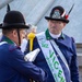 Two men in formal military-style uniforms of the Associazione Nazionale Alpini (Italian Alpine troops veterans association) are engaged in conversation. The man on the right wears a sash identifying him as a representative of the Vicenza section, specifically the 'Monte Pasubio' group. They appear to be at an official Alpini gathering or parade event.
