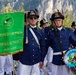 A ceremonial parade or gathering of the Associazione Nazionale Alpini, specifically the 'Fanfara Storica Monte Pasubio' band from the Sezione di Vicenza. Members are dressed in traditional Alpini uniforms consisting of blue jackets, white trousers, and characteristic black hats with feathers. The event appears to take place outdoors against a mountainous backdrop.