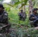 Three armed soldiers are positioned in a dense tropical jungle environment with banana trees and lush vegetation. At least two of the soldiers display Japanese flag patches on their uniforms, identifying them as members of the Japan Ground Self-Defense Force (JGSDF). The soldiers appear to be conducting a patrol or tactical exercise in a jungle terrain.