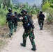 A group of armed military or special operations personnel are conducting a patrol along a dirt trail through a tropical jungle environment. The soldiers are wearing camouflage uniforms with tactical vests and helmets, carrying assault rifles in a ready position. The vegetation and uniform patterns suggest a Southeast Asian operational context.