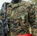 A U.S. Marine is shown from the neck down wearing Marine Pattern (MARPAT) woodland digital camouflage uniform. The Marine is carrying a rifle with a scope and has a service medal pinned to their chest. The name tape reads 'ABORNE' and the branch tape reads 'U.S. MARINES'.