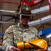 A U.S. Army Sergeant named Gulley, wearing an OCP (Operational Camouflage Pattern) uniform and a Drill Sergeant campaign hat, sits inside a boxing ring examining a pair of gold/yellow boxing gloves. His uniform displays a U.S. Army tape, name tape, Staff Sergeant rank chevrons, an American flag patch, and what appears to be a unit patch. The setting is a boxing gym with Everlast-branded ropes and equipment visible in the background.