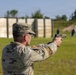 A U.S. Army soldier in Operational Camouflage Pattern (OCP) uniform is firing a pistol at a military shooting range. The soldier is in a two-handed shooting stance, aiming at multiple silhouette targets downrange. The setting appears to be an outdoor live-fire training range with wooden barriers and a berm in the background.
