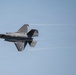 A single stealth fighter jet, consistent with an F-35 Lightning II, is captured in flight against a clear blue sky. The aircraft is viewed from a slightly elevated angle, showing its top surface with condensation trails streaming from its wingtips. The image is sharp and well-exposed, suggesting a professional aviation or airshow photograph.