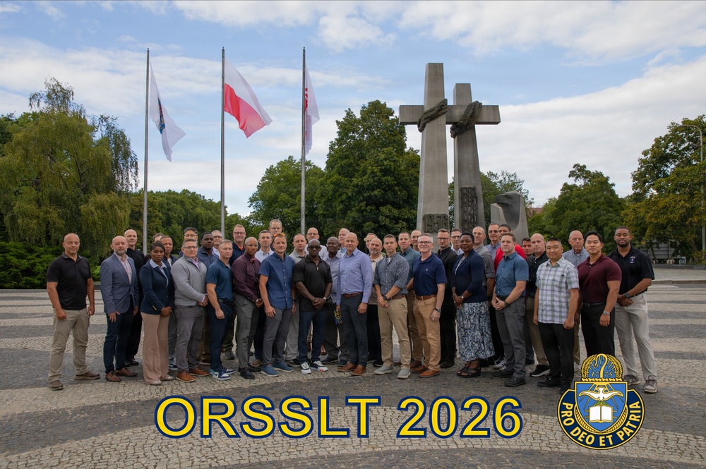 A group photograph of approximately 40 individuals posing in front of a large monument featuring three crosses, likely the Three Crosses Monument in Poznań, Poland. The image is labeled 'ORSSLT 2026' with a military chaplain insignia bearing the motto 'Pro Deo Et Patria' (For God and Country). The group appears to be military chaplains or chaplain candidates gathered for a training or leadership program.