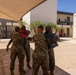 Military personnel in MARPAT camouflage uniforms are gathered in an outdoor courtyard area, with several individuals embracing in what appears to be a celebratory or farewell occasion. Two pairs of service members are hugging in the foreground, with one individual holding a dark blue folder or certificate binder. The setting appears to be a U.S. Marine Corps installation, identifiable by building number 507 visible in the background.