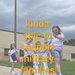 A group of children and an adult woman are participating in a military family support event, walking along a sidewalk outside a brick building. The participants are wearing matching purple tie-dye shirts, and two children are holding a hand-decorated sign reading 'Military Child.' Overlaid text reads 'kinda chic to support military families.'