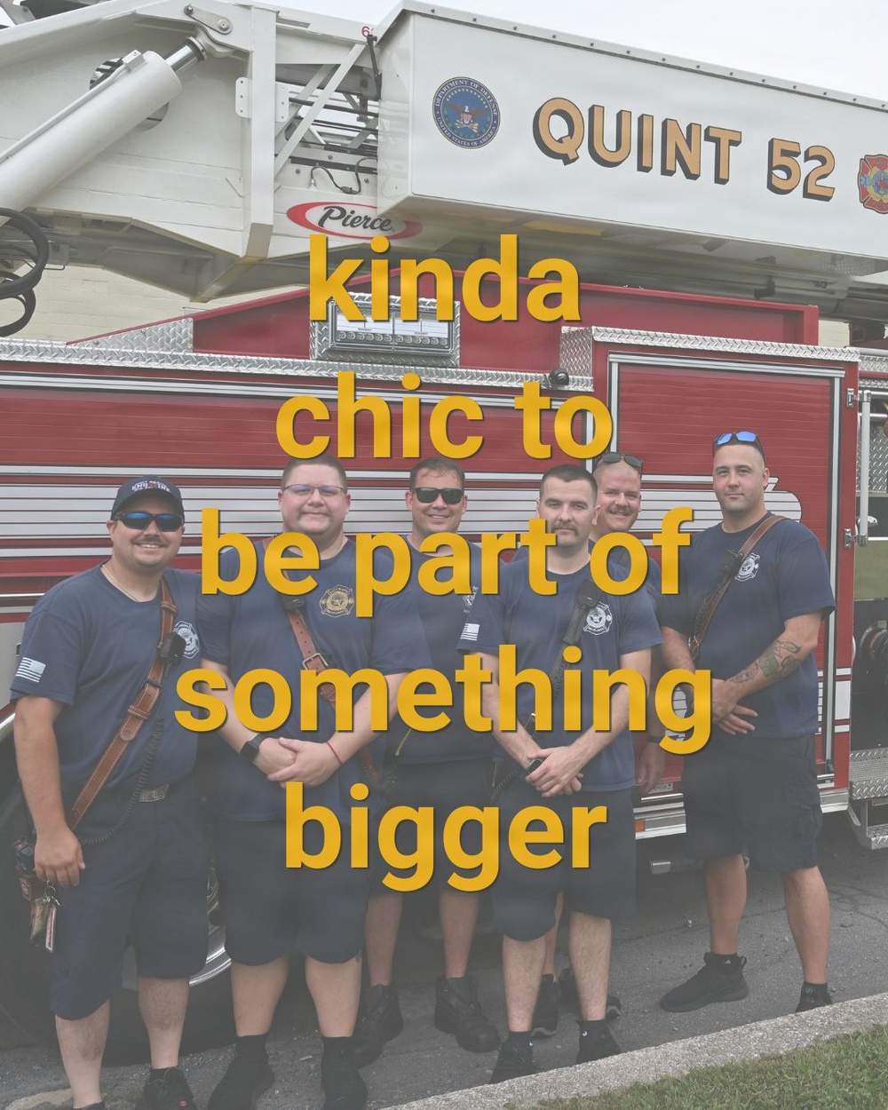 A group of seven firefighters in navy blue uniforms pose together in front of a red Pierce fire apparatus labeled 'Quint 52'. The image includes overlaid yellow text reading 'kinda chic to be part of something bigger'. The photo appears to be a team or crew photo, likely taken at a fire station.
