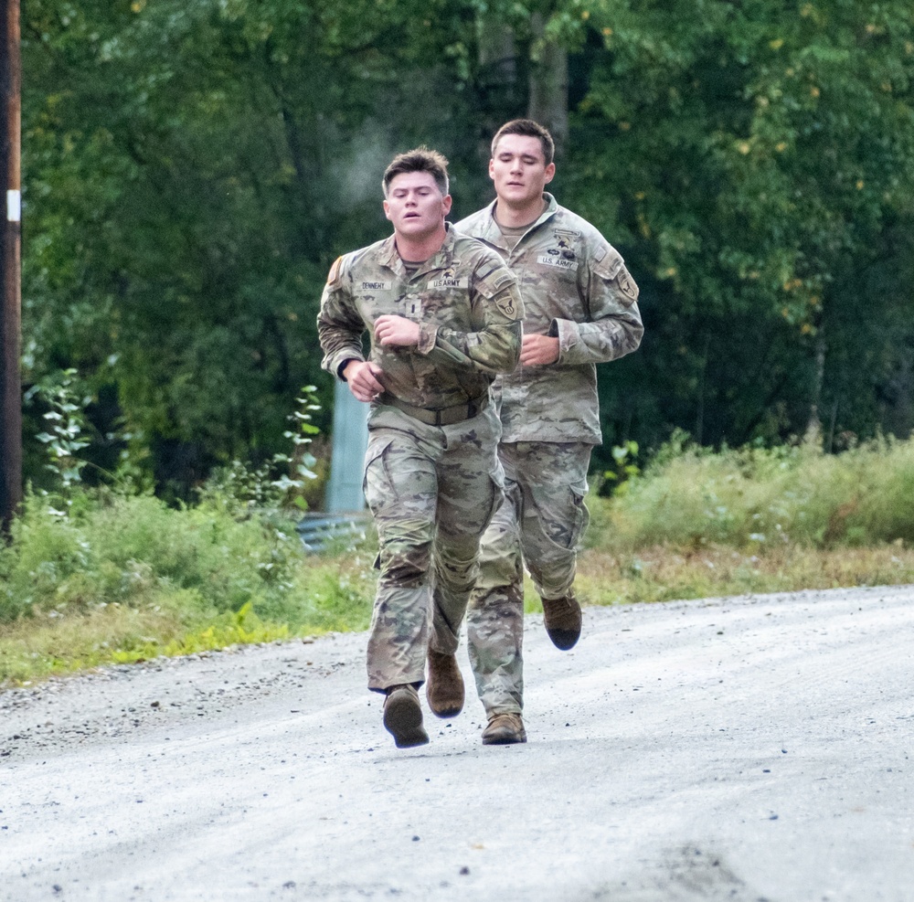 Two U.S. Army soldiers in OCP (Operational Camouflage Pattern) uniforms are running together on a gravel road. The soldier on the left has a name tape reading 'TENNERY' and both wear 'U.S. ARMY' chest tapes with unit patches on their sleeves. They appear to be conducting a physical fitness run or military training exercise in a wooded outdoor environment.