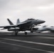A U.S. Navy F/A-18 Super Hornet (bureau number 112) is captured launching or landing on an aircraft carrier flight deck. The image is taken with a panning technique, creating motion blur in the background while keeping the aircraft relatively sharp. The overcast sky and dark non-skid flight deck surface are characteristic of carrier operations at sea.