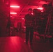 A person is standing in a storage room or warehouse bathed in red lighting, carrying a box of Hammermill 'Great White 30' copy paper. The space is densely packed with stacked boxes of the same paper brand on shelving units. The red-tinted fluorescent lighting creates a dramatic, moody atmosphere throughout the storage area.