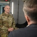 A U.S. Army soldier named Miller, wearing OCP (Operational Camouflage Pattern) uniform, is seated and participating in what appears to be a formal interview or media engagement. He is facing another individual whose back is to the camera, suggesting an interviewer-interviewee setup. The setting includes professional lighting equipment consistent with a media or press interview environment.