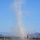 Canopy Relative Work Teams Compete at 2026 National Championships A dust devil — a small, rotating column of dust and debris — rises vertically from an arid, flat terrain in what appears to be a desert or semi-arid region. The scene includes colorful event flags in the foreground, suggesting a nearby outdoor event or venue. A mountain range is visible in the background under a clear blue sky.