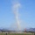 Canopy Relative Work Teams Compete at 2026 National Championships A dust devil or small whirlwind is visible rising from an open field at what appears to be an airfield or recreational flying area. The column of dust and debris extends high into a clear blue sky, with mountain ranges visible in the background. Orange marker flags and windsocks are positioned across the field, suggesting an organized aviation or kite-flying event.