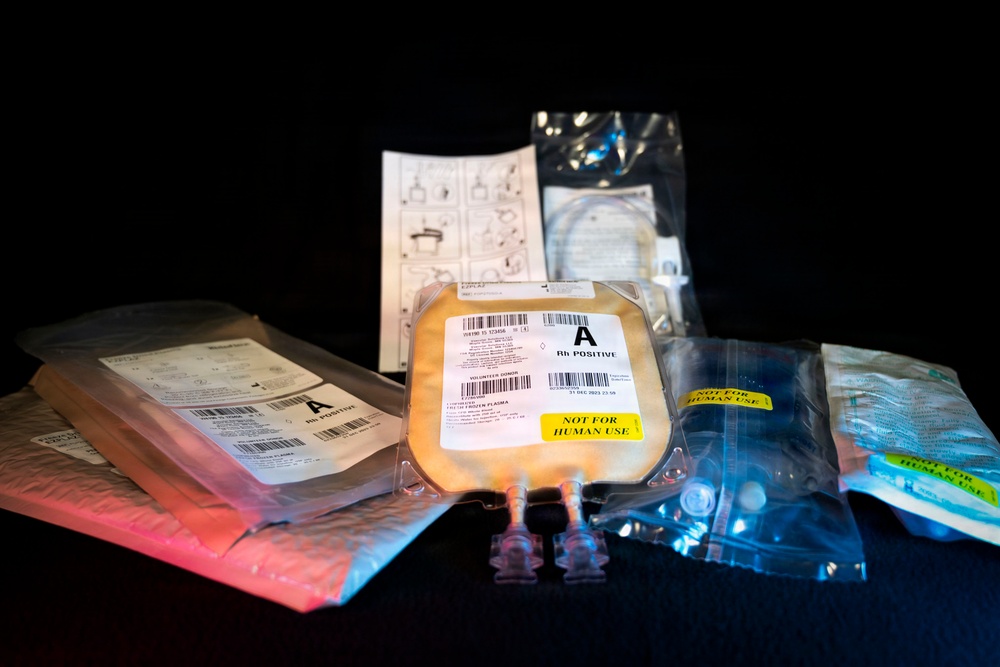 The image shows multiple medical plasma bags labeled 'A Rh Positive' arranged on a dark surface under dramatic lighting. The central bag is prominently labeled 'NOT FOR HUMAN USE' with a yellow sticker, indicating these are likely training, research, or quality control samples. Associated medical packaging, tubing, and instructional materials are also visible.