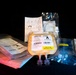 The image shows multiple medical plasma bags labeled 'A Rh Positive' arranged on a dark surface under dramatic lighting. The central bag is prominently labeled 'NOT FOR HUMAN USE' with a yellow sticker, indicating these are likely training, research, or quality control samples. Associated medical packaging, tubing, and instructional materials are also visible.