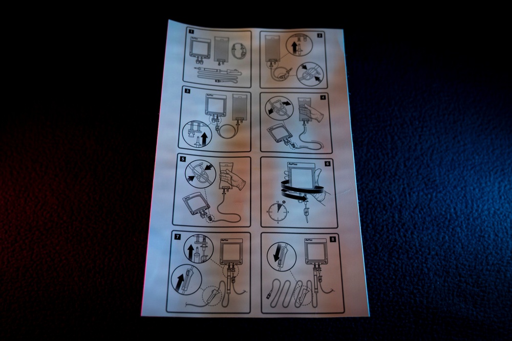 The image shows a printed instruction sheet with 8 numbered sequential steps for assembling or operating a medical or technical device, likely an IV infusion set or similar fluid delivery system. The sheet contains black-and-white line drawings arranged in a 2x4 grid layout. The paper is photographed on a dark surface under mixed lighting conditions.