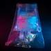 The image shows a sealed medical IV bag or infusion pouch, manufactured by B. Braun, photographed under dramatic pink and blue lighting against a dark background. The transparent outer packaging contains an inner IV bag with visible tubing and connectors. The expiration date visible on the label reads 12/23, and a LOT number is partially visible.